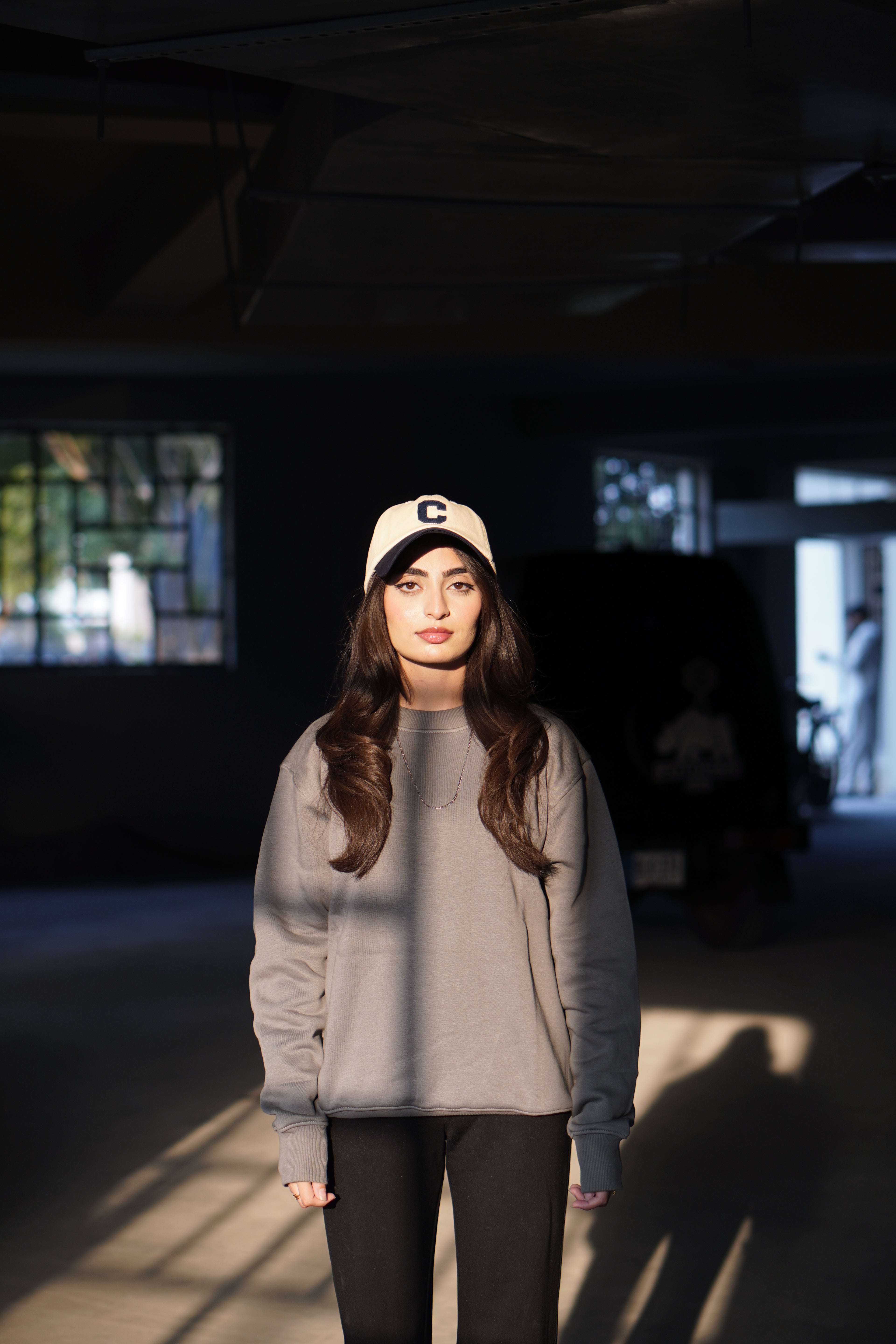 Woman wearing a gray hoodie  and black pants standing in a dimly lit room with stained glass windows.
