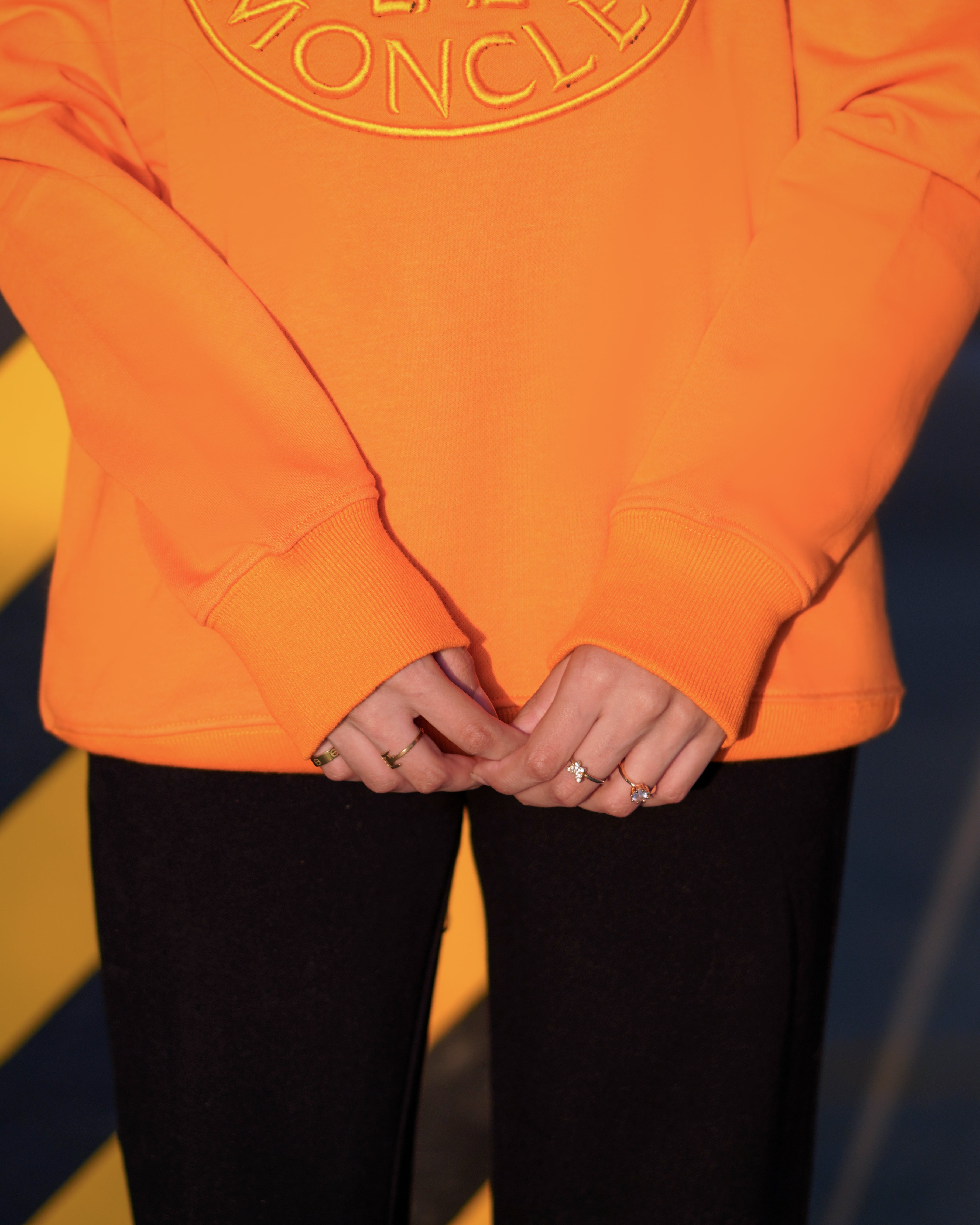 Person wearing an orange hoodie with a logo, standing against a colorful background.